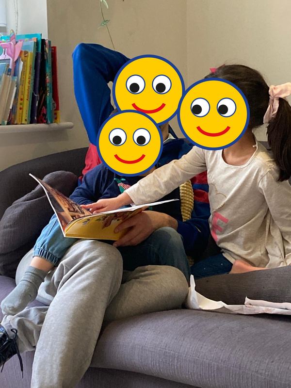 Un papá y dos niños leyendo el libro en un sofá, con caritas dibujadas sobre sus rostros
